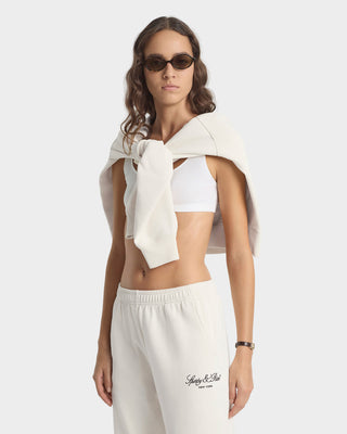 Woman wearing a white sleeveless top with a bow and white pants on a light gray background