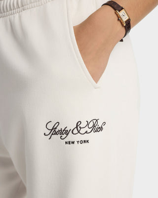 White sweatpants with 'Sporty & Rich New York' logo and a watch on a wrist.