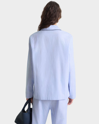 Person wearing a light blue pinstripe suit holding a black handbag on a white background