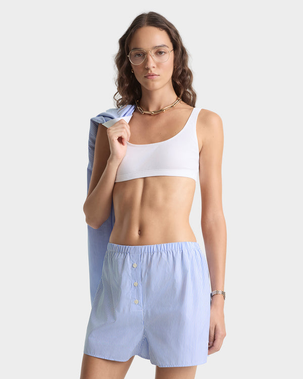Woman wearing a white sports bra and light blue striped shorts on a plain background