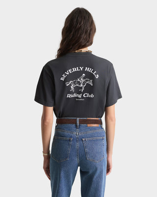Person wearing a black t-shirt with 'Beverly Hills Riding Club' text and graphic on the back, standing against a white background.