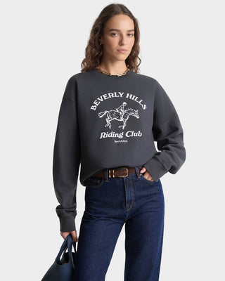 Person wearing a dark gray sweatshirt with 'Beverly Hills Riding Club' text and graphic, standing against a plain background.