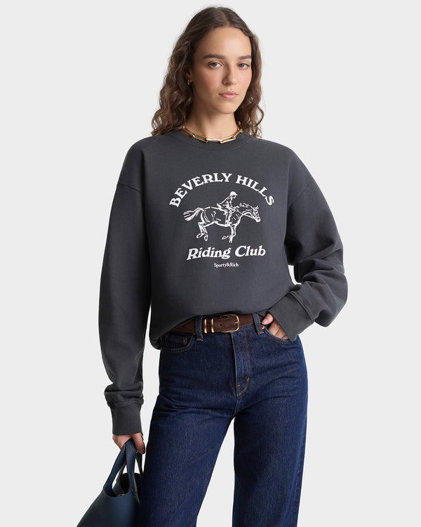 Person wearing a dark gray sweatshirt with 'Beverly Hills Riding Club' text and graphic, standing against a plain background.