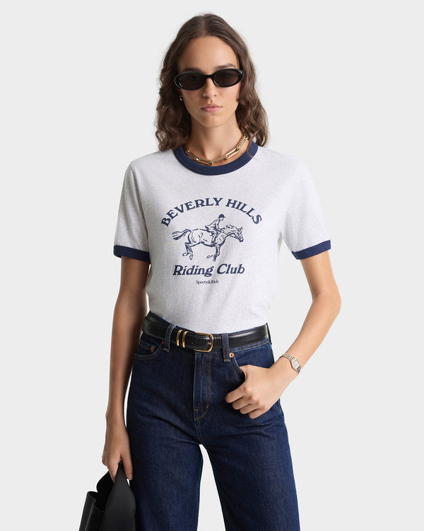 Woman wearing a 'Beverly Hills Riding Club' t-shirt with sunglasses and jeans on a white background