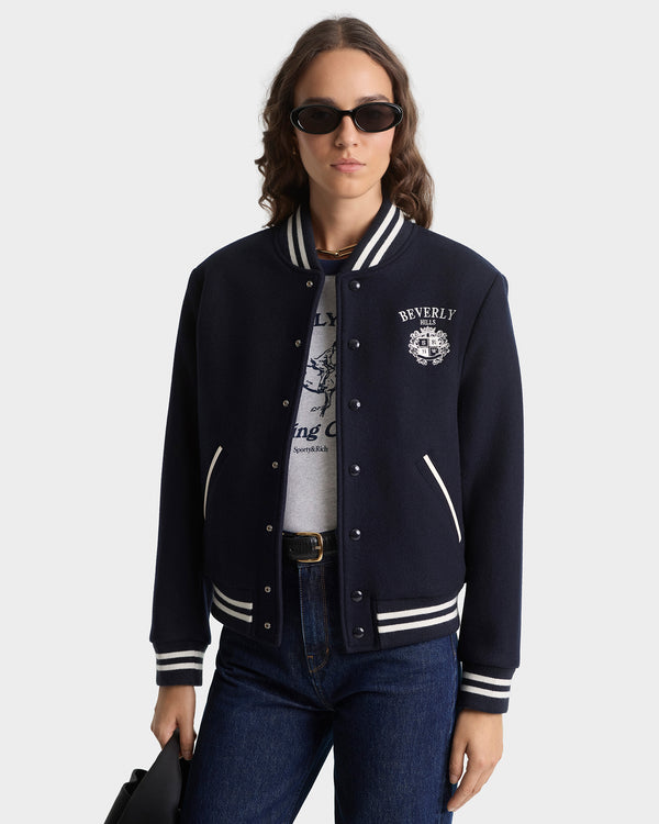 Person wearing a navy varsity jacket with white accents on a plain background