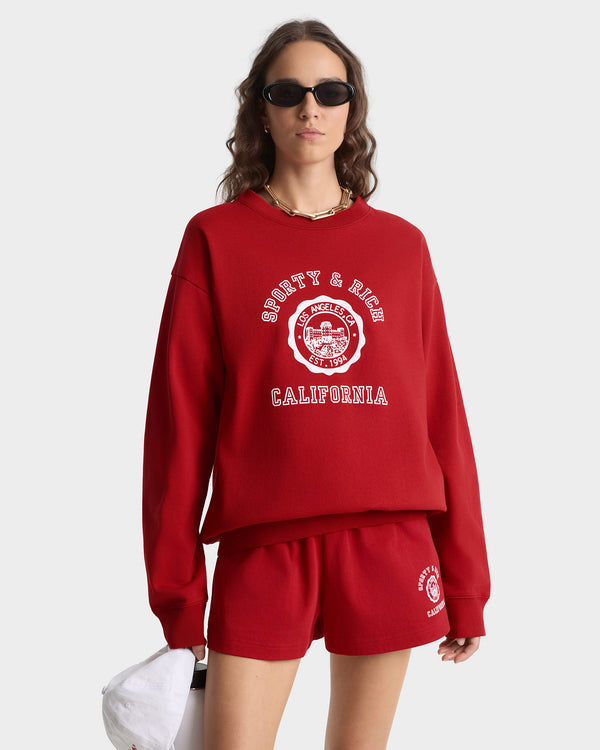 Person wearing a red 'Sports & Rich California' sweatshirt and shorts set on a white background