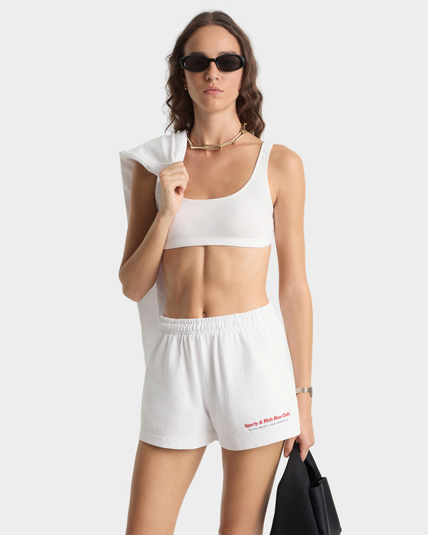 Woman wearing a white sports bra and shorts with sunglasses on a white background