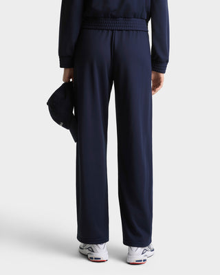 Person wearing a navy tracksuit with white sneakers on a light gray background