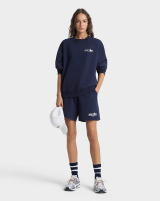Person wearing navy blue sweatshirt and shorts with a logo, holding a white helmet on a white background