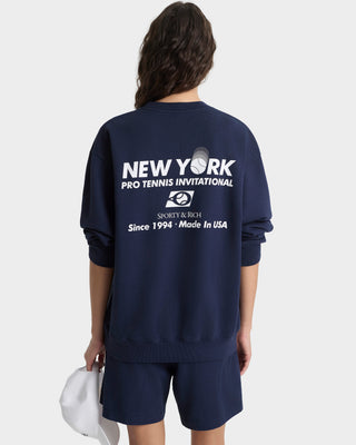 Person wearing a navy blue sweatshirt with 'New York Pro Tennis Invitational' text on the back, standing against a white background.