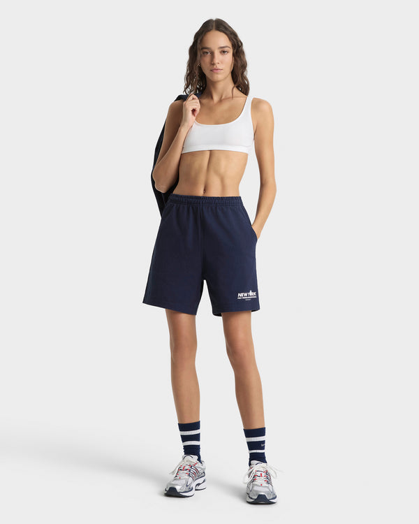 Woman wearing navy athletic shorts with a logo on a white background