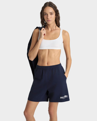 Woman wearing a white sports bra and navy shorts with a visible brand logo on a white background