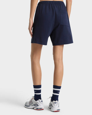 Person wearing navy shorts and white sneakers with red accents on a white background