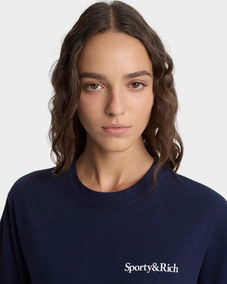 Person wearing a navy blue sweatshirt with 'Sporty&Rich' logo on a light gray background