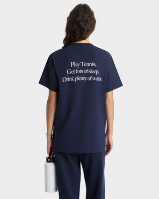 Person wearing a navy blue t-shirt with text on the back, holding a white water bottle.