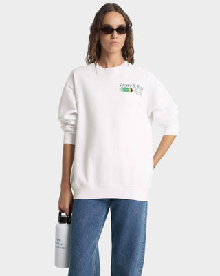 Person wearing a white sweatshirt with a logo, holding a water bottle on a plain background