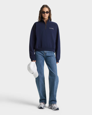 Person wearing a navy blue sweater and jeans holding a white hard hat on a light gray background