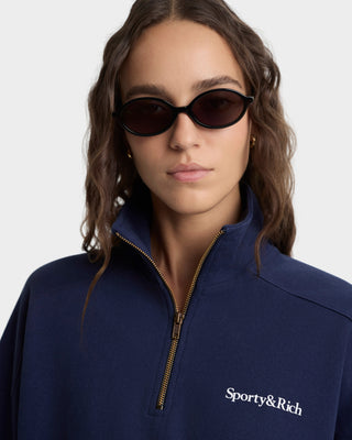 Woman wearing sunglasses and a navy blue jacket with 'Sporty&Rich' logo on a white background