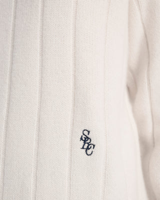 Close-up of a white sweater with a small logo on the chest.