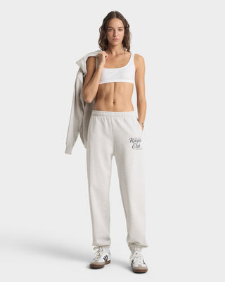 Woman wearing a white sports bra and beige sweatpants with 'Rogue Club' logo on a white background