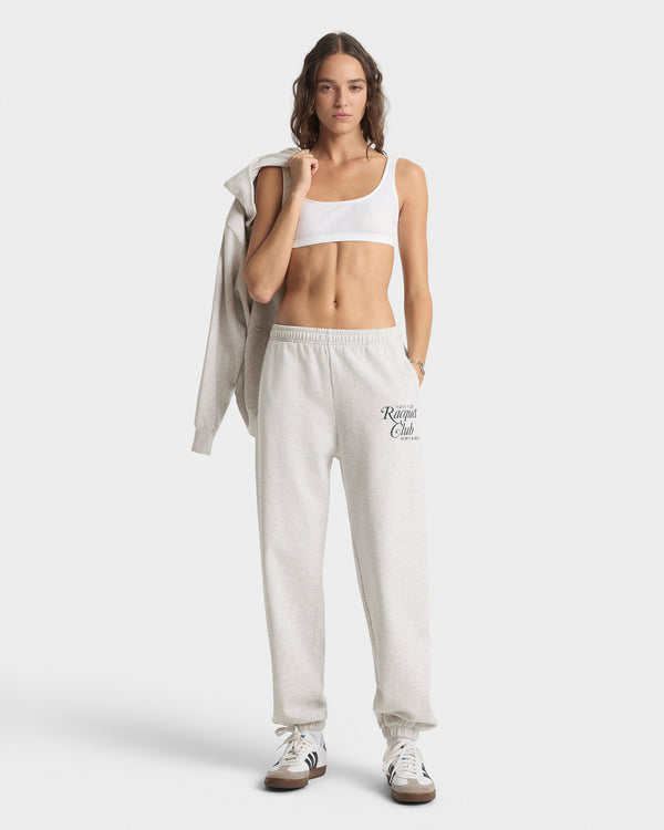 Woman wearing a white sports bra and beige sweatpants with 'Rogue Club' logo on a white background