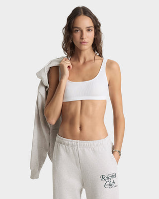 Woman wearing a white sports bra and gray sweatpants with a visible brand logo on a white background