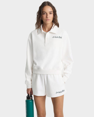 Woman wearing a white outfit with branding, holding a green water bottle on a white background