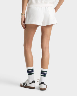 Person wearing white socks with dark stripes and Adidas shoes on a plain background