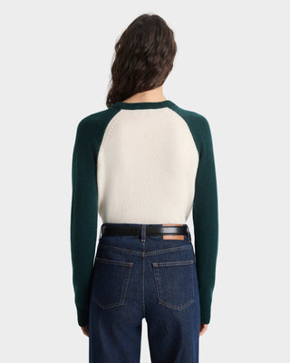 Person wearing a green and cream long-sleeve shirt with dark jeans on a white background