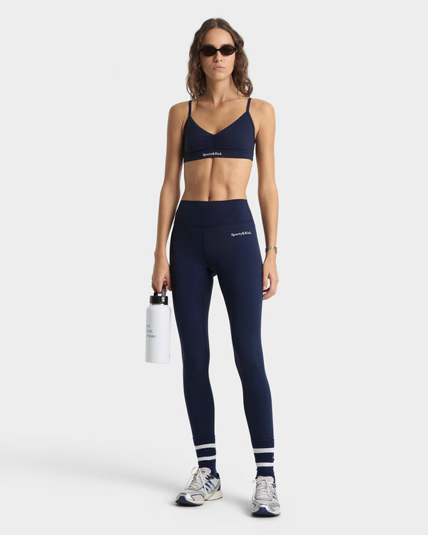 Woman wearing navy sports bra and leggings with a white background