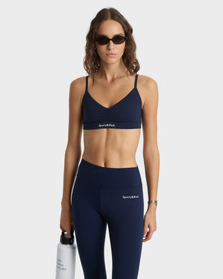 Woman wearing navy sports bra and leggings with 'Sporty & Rich' branding, holding a water bottle.