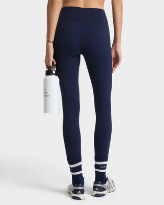 Person wearing navy leggings with white accents, holding a white water bottle on a white background