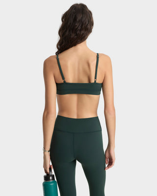 Person wearing a green sports bra and leggings holding a water bottle on a white background