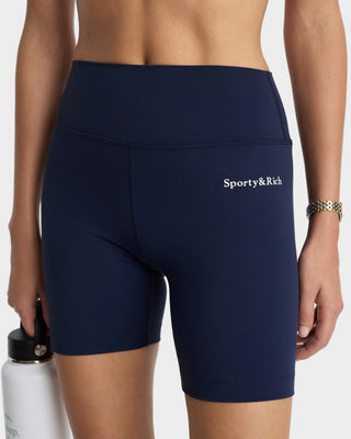 Navy blue athletic shorts with 'Sporty & Rich' logo worn by a person, holding a white water bottle.