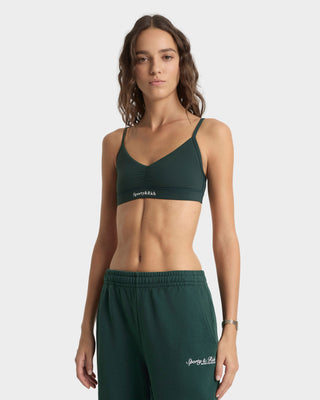 Woman wearing a green sports bra and shorts with branding on a white background