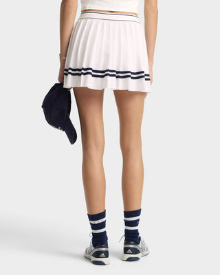 Person wearing a white skirt with black stripes, navy socks, and Adidas shoes on a white background