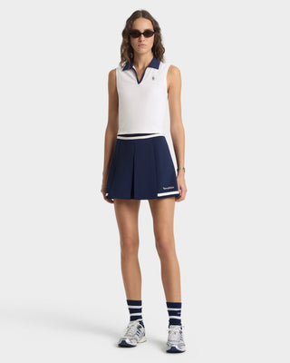 Woman wearing a white sleeveless top and navy skirt with visible branding on a white background