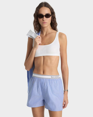 Woman wearing a white sports bra and blue shorts on a white background