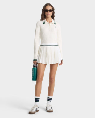 Woman in a white tennis outfit with a skirt, holding a green bag on a white background