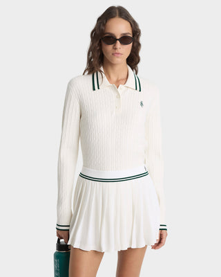 Woman wearing a white ribbed long-sleeve top and skirt with green accents on a white background