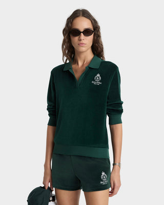 Woman wearing a green polo shirt and shorts with a logo, holding a green bag on a white background