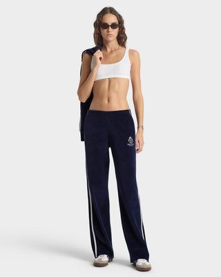 Woman wearing navy track pants with white stripes and a white sports bra on a white background