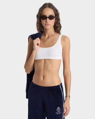 Woman wearing a white sports bra and navy tracksuit on a white background