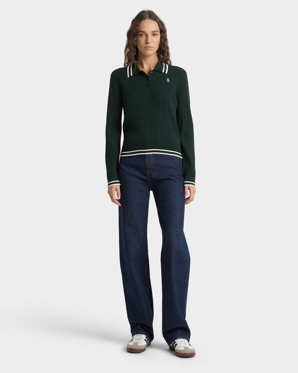 Woman wearing a green sweater with white trim and dark blue pants on a white background