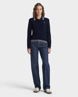 Person wearing a navy sweater with white trim and dark blue jeans on a white background
