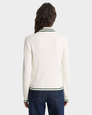 Person wearing a white ribbed sweater with greeb trim and blue jeans on a white background