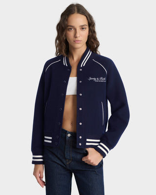 Woman wearing a navy blue varsity jacket with white accents on a white background