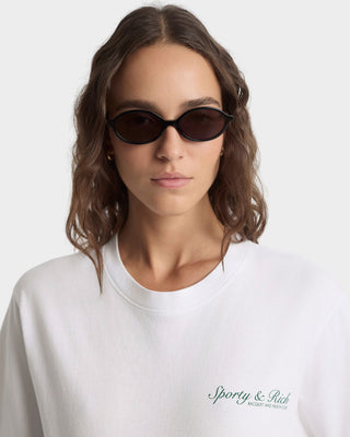 Person wearing dark sunglasses and a white sweatshirt with 'Sporty & Rich' branding on a light background