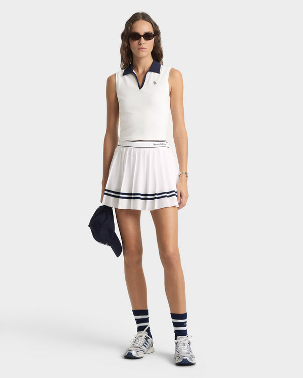 Woman wearing a white tennis dress with navy accents on a white background
