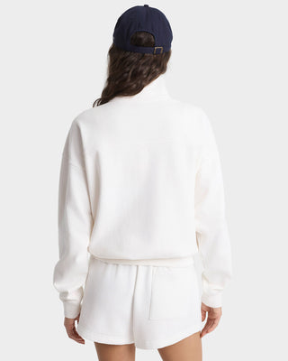 Person wearing a white sweater and white shorts with a navy cap on a white background